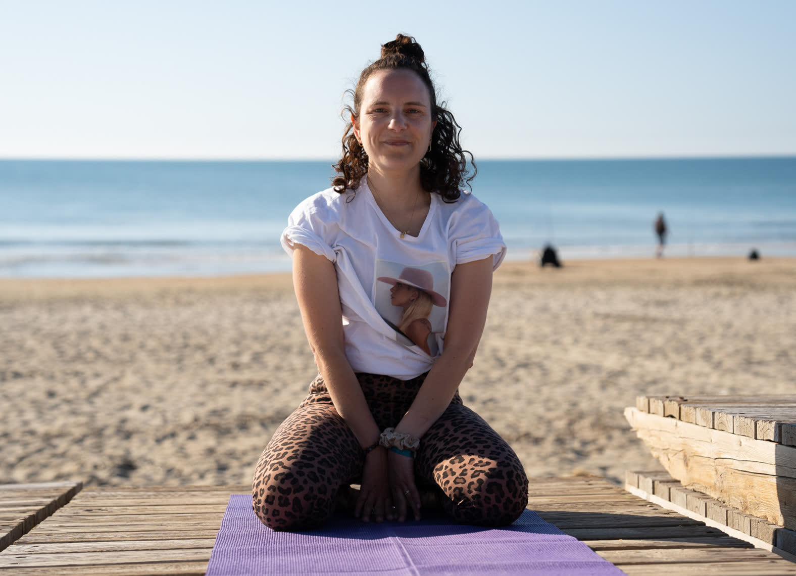 Madeline souriante, assise sur son tapis face à la mer